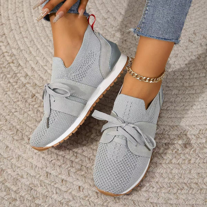 Scarpe da ginnastica grigie da donna, design moderno con lacci, suola bianca e dettagli in maglia, indossate con jeans e cavigliera dorata.