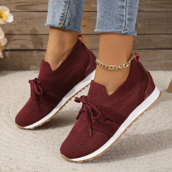 Scarpe da ginnastica rosse da donna, design in maglia traspirante, suola bianca, indossate con jeans. Stile casual e moderno.