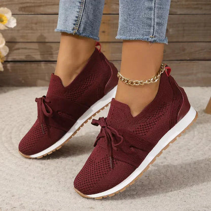 Scarpe da ginnastica rosse da donna, design in maglia traspirante, suola bianca, indossate con jeans. Stile casual e moderno.