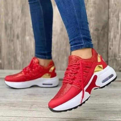 Scarpe da ginnastica rosse e oro su pavimento in legno, indossate con jeans aderenti. Design moderno, suola bianca, perfette per moda casual e sportiva.