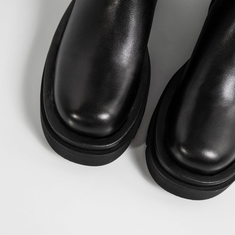 Stivali neri in pelle lucida su sfondo bianco, moda autunno inverno, calzature eleganti, tendenza scarpe donna, design minimalista.