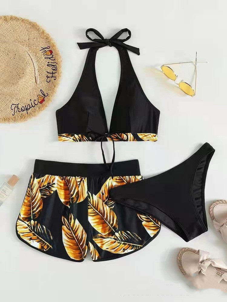 Bikini nero con foglie tropicali gialle, occhiali da sole, cappello di paglia e sandali estivi. Moda mare donna, abbigliamento estivo trendy.