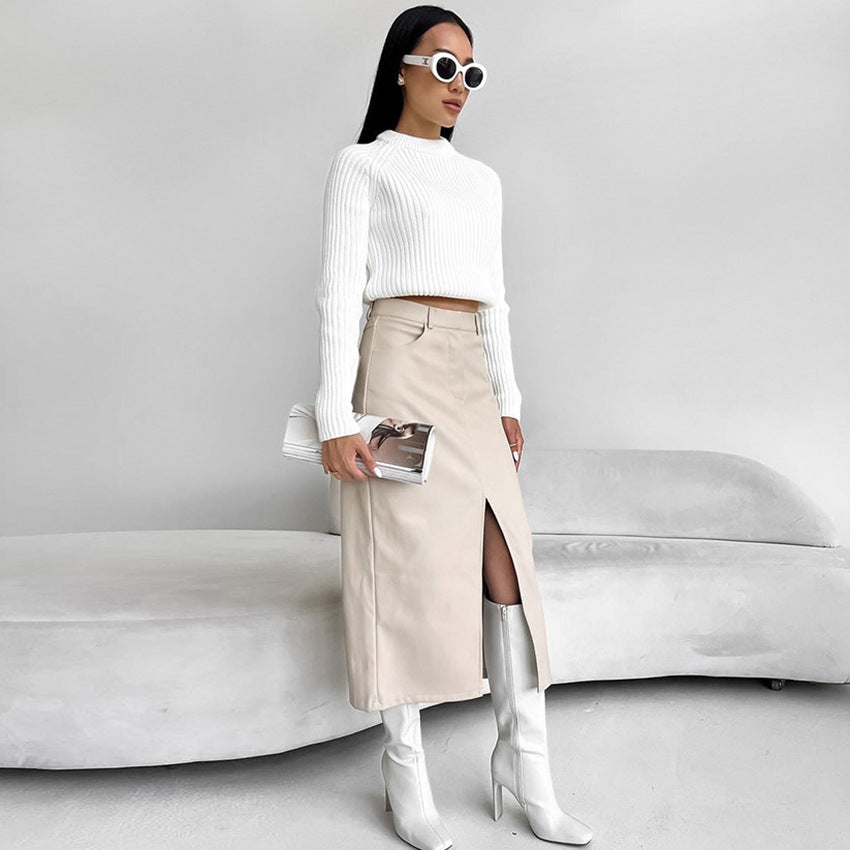 Donna con occhiali da sole bianchi indossa maglione bianco, gonna beige con spacco e stivali alti bianchi. Moda elegante e minimalista.