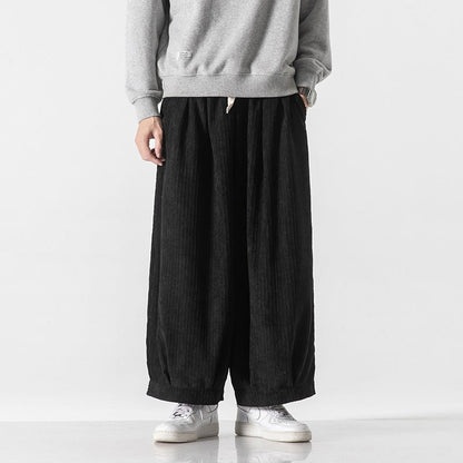 Pantaloni larghi neri in velluto a coste, indossati con felpa grigia e scarpe da ginnastica bianche. Moda casual uomo, stile urbano moderno.