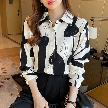 Donna con camicia bianca e nera astratta, seduta in un ambiente moderno. Moda elegante, abbigliamento femminile, stile contemporaneo.