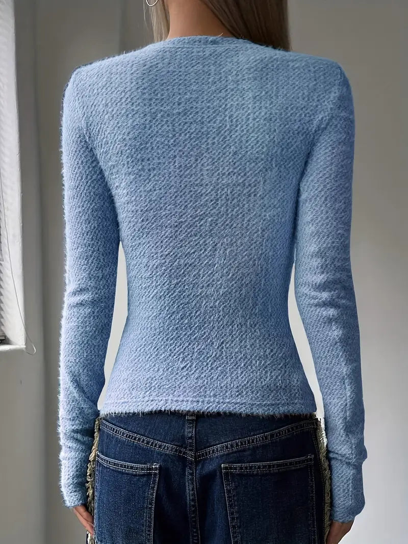 Donna di spalle con maglione azzurro in lana, jeans a vita alta, in una stanza luminosa. Moda autunnale, abbigliamento casual elegante.