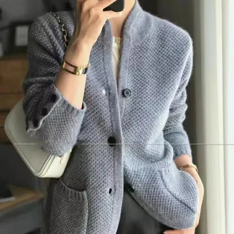 Donna con cardigan grigio a maglia grossa, borsa bianca a tracolla, bracciali dorati. Moda autunnale elegante e casual.