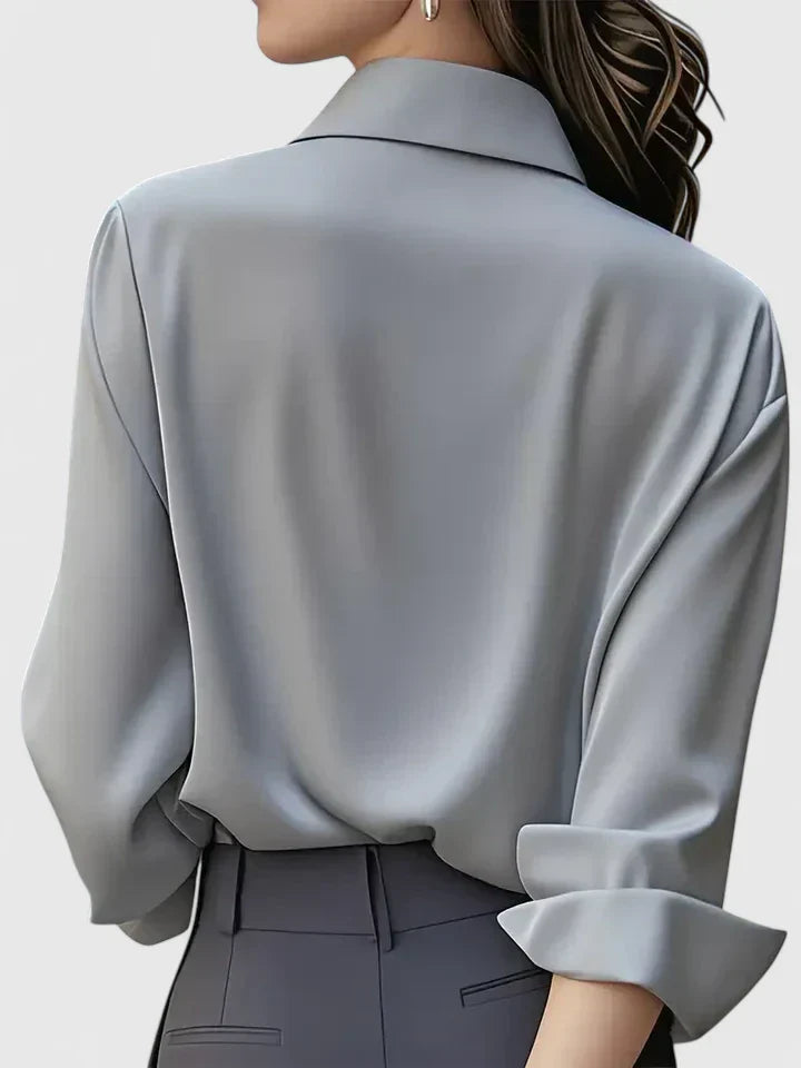 Donna di spalle con camicia di seta grigia, maniche arrotolate, abbinata a pantaloni eleganti. Moda femminile, abbigliamento elegante, stile sofisticato.