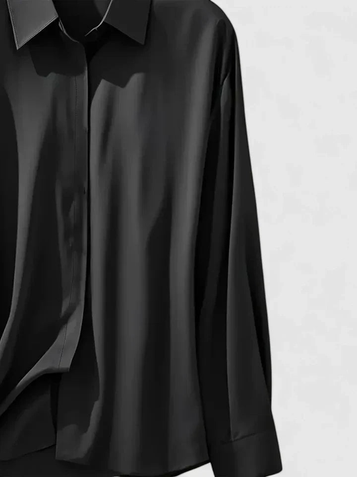 Camicia nera in seta lucida, maniche lunghe, colletto classico, su sfondo grigio chiaro. Elegante e moderna, ideale per moda autunnale.