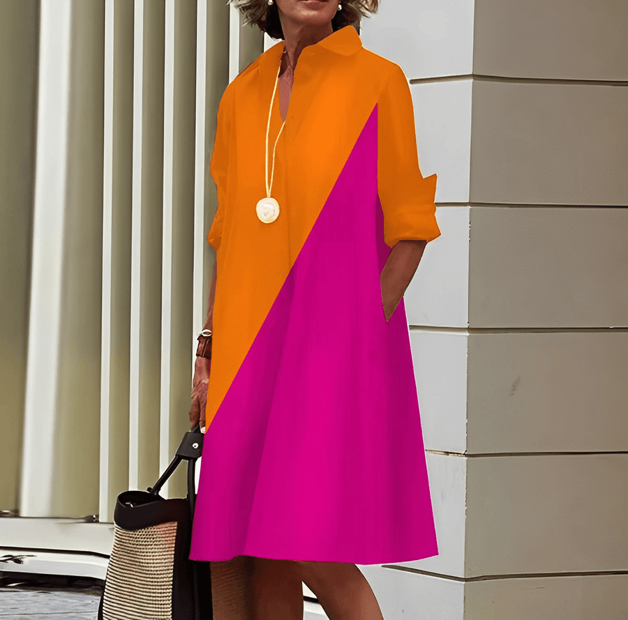Donna con abito color block arancione e fucsia, accessoriato con collana bianca e borsa di paglia. Moda estiva, abbigliamento casual chic.