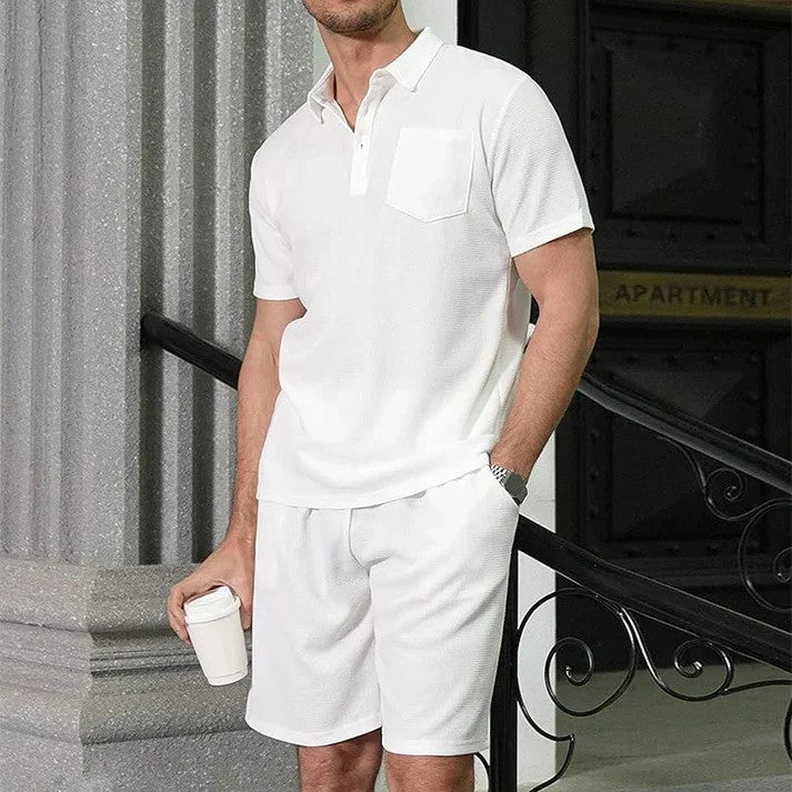 Uomo in completo estivo bianco, polo e pantaloncini, con caffè in mano. Moda casual maschile, abbigliamento estivo elegante.
