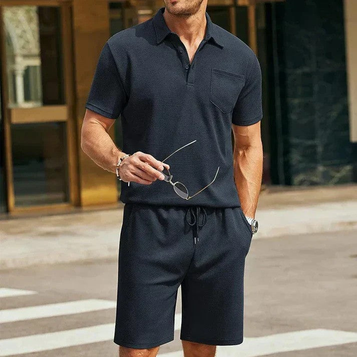 Uomo in abbigliamento casual estivo, indossa polo e pantaloncini neri, tiene occhiali da sole. Moda maschile elegante e moderna in città.