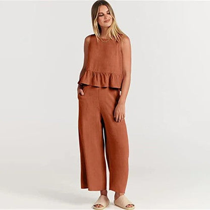 Donna in tuta marrone con volant, posa su sfondo bianco. Moda femminile, abbigliamento casual elegante, pantaloni larghi, top senza maniche.
