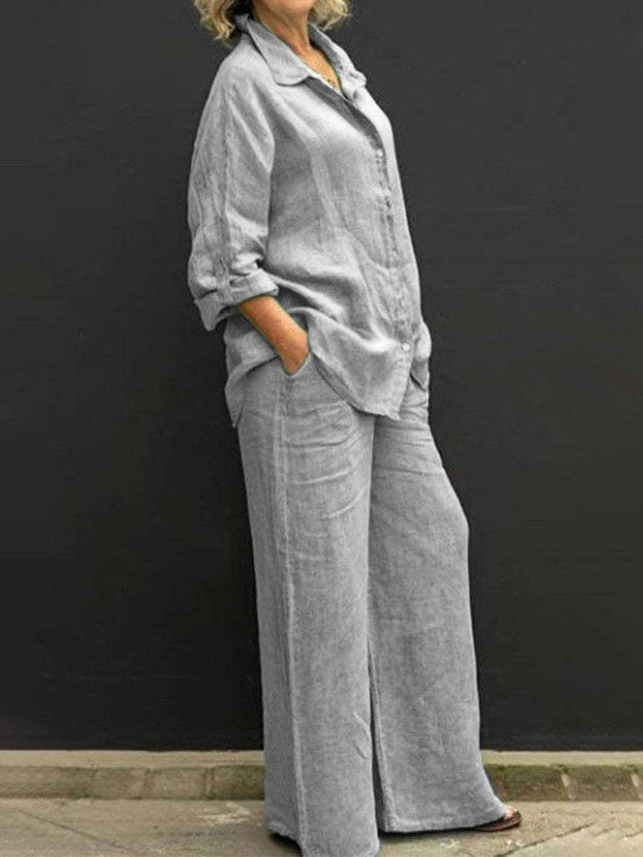 Donna in abbigliamento casual grigio, camicia e pantaloni larghi di lino, posa contro sfondo nero. Moda donna, stile rilassato, outfit estivo.