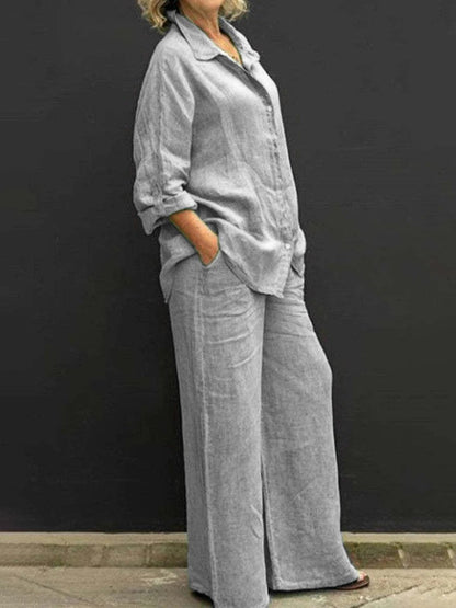 Donna in abbigliamento casual grigio, camicia e pantaloni larghi di lino, posa contro sfondo nero. Moda donna, stile rilassato, outfit estivo.