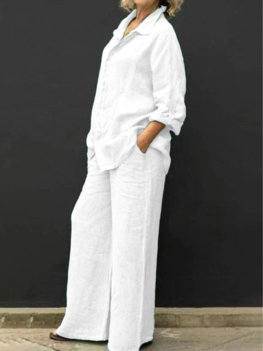 Donna in abbigliamento estivo bianco, camicia e pantaloni larghi, posa contro sfondo nero. Moda casual, stile elegante, comfort estivo.