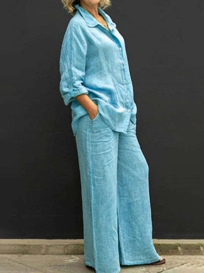 Donna in abbigliamento casual, indossa un completo di lino azzurro con camicia e pantaloni larghi, sfondo nero. Moda estiva, stile rilassato.