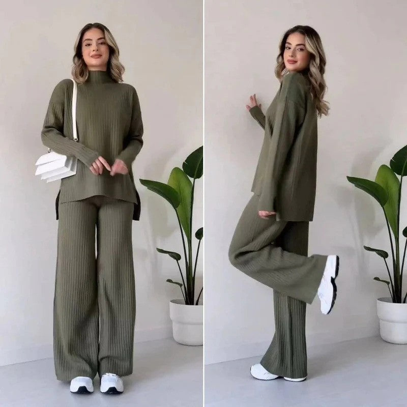 Donna in completo maglia verde oliva, maglione e pantaloni larghi, con borsa bianca e sneakers, posa davanti a piante d'appartamento.