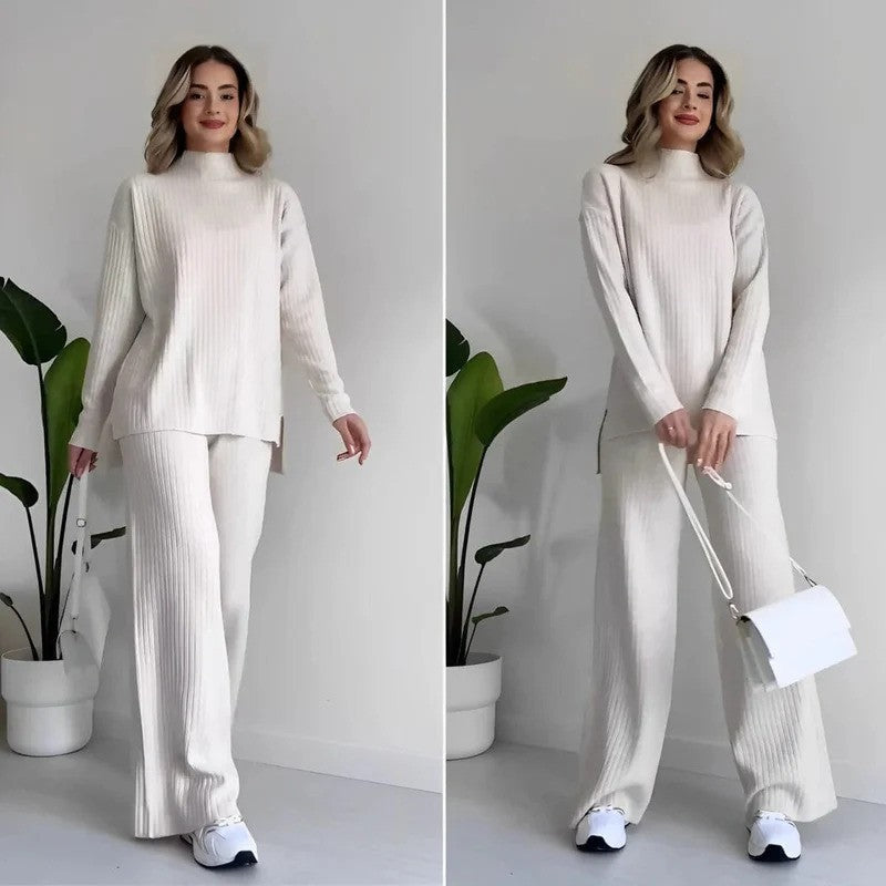 Donna in abbigliamento casual beige, maglione e pantaloni a coste, con borsa bianca e scarpe da ginnastica, piante verdi sullo sfondo.