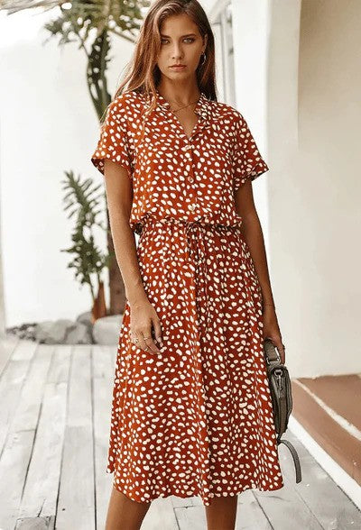 Donna con abito midi a pois marrone e bianco, in posa su una veranda. Moda estiva, abbigliamento casual elegante, tendenze 2023.