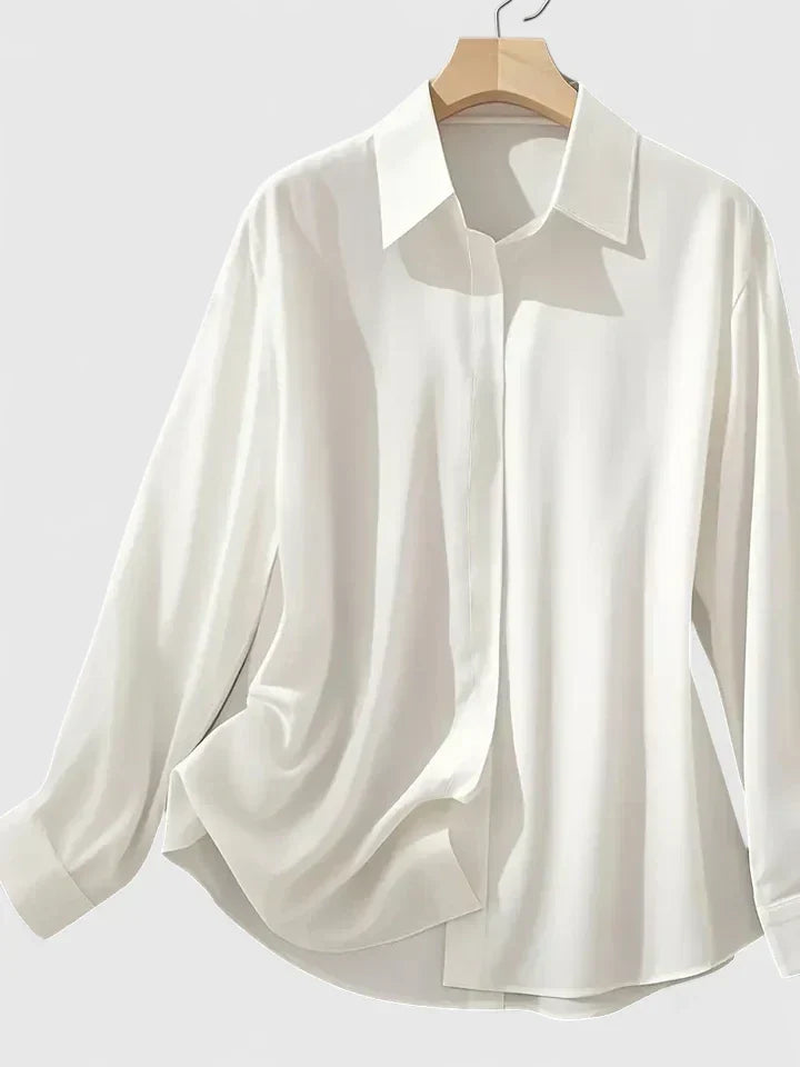 Camicia bianca elegante in seta su gruccia, maniche lunghe, colletto classico. Moda donna, abbigliamento formale, tessuto liscio e lucido.