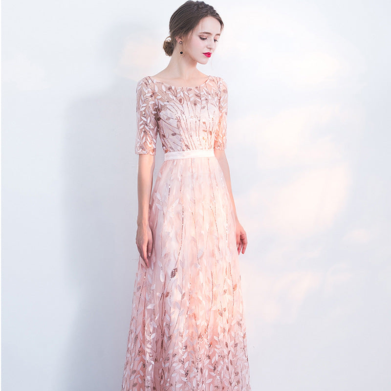 Abito da sera elegante rosa chiaro con dettagli floreali, maniche a tre quarti, indossato da una donna su sfondo bianco. Moda femminile raffinata.