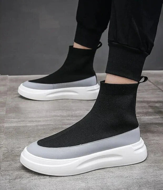 Scarpe da ginnastica alte nere e grigie su pavimento grigio, design moderno con suola bianca spessa, moda calzature uomo, stile casual elegante.
