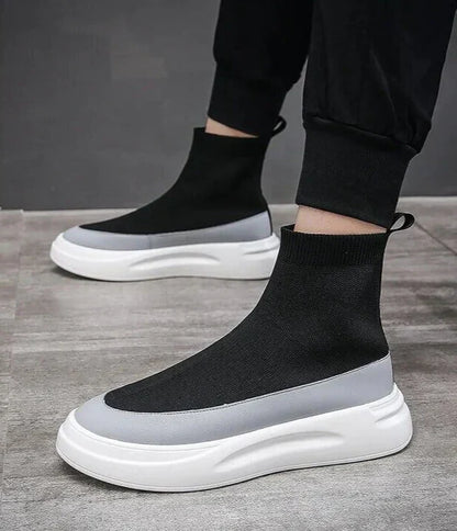 Scarpe da ginnastica alte nere e grigie su pavimento grigio, design moderno con suola bianca spessa, moda calzature uomo, stile casual elegante.