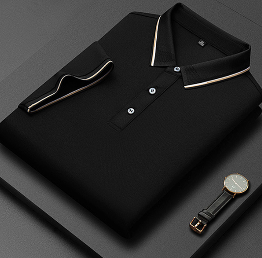 Camicia polo nera piegata con colletto a contrasto, bottoni bianchi, su sfondo grigio. Orologio elegante con cinturino in pelle accanto.