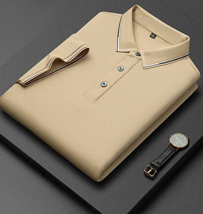 Camicia polo beige piegata su sfondo nero, con colletto a contrasto e tre bottoni, accanto a un orologio elegante con cinturino in pelle nera.