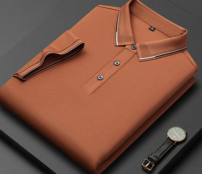 Camicia polo arancione piegata su sfondo nero, con colletto a contrasto e tre bottoni, accanto a un orologio elegante con cinturino in pelle.