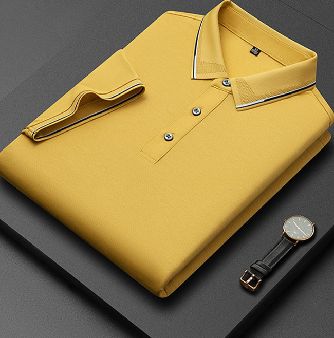 Camicia polo gialla piegata su sfondo grigio, con colletto a contrasto e orologio da polso nero accanto. Moda uomo, abbigliamento casual elegante.