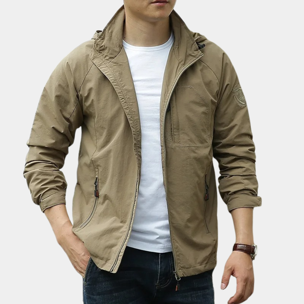 Giacca a vento beige da uomo, stile casual, con zip frontale e tasche laterali, indossata su maglietta bianca e jeans. Moda maschile autunnale.