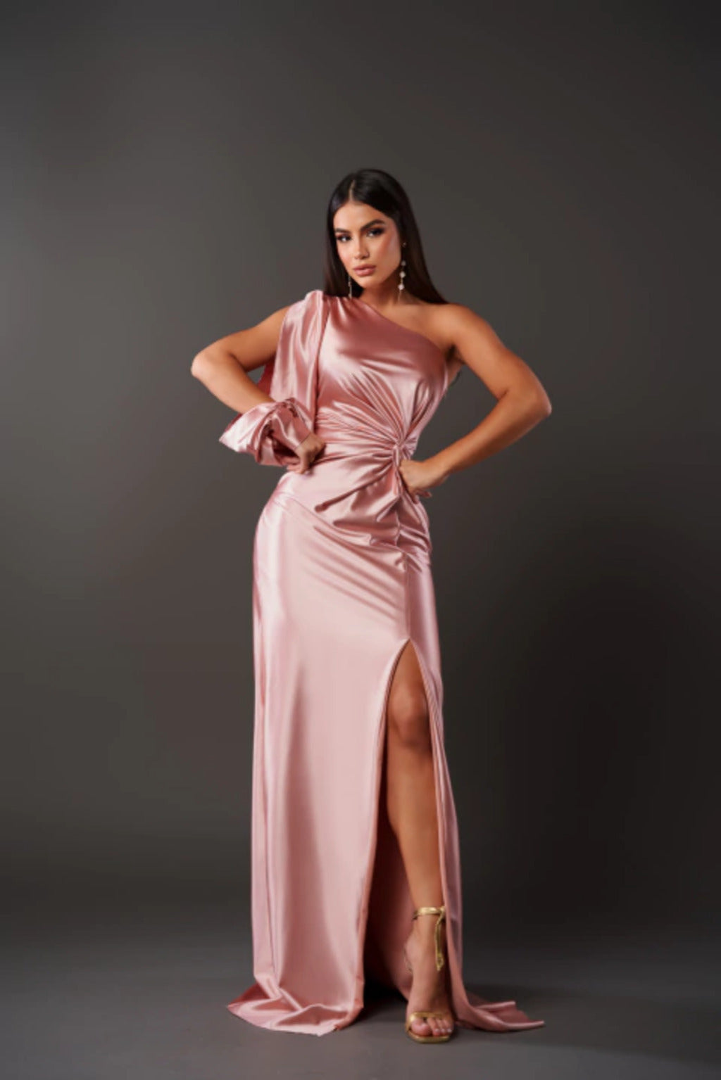 Donna in abito da sera rosa satinato con spacco alto, posa elegante su sfondo grigio. Moda femminile, abbigliamento elegante, tendenze 2023.