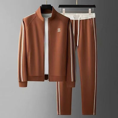 Tuta sportiva marrone con giacca e pantaloni, dettagli a righe bianche, logo sul petto. Abbigliamento casual elegante per uomo.