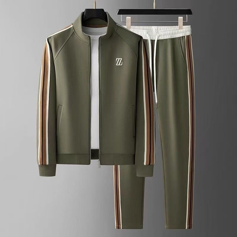 Tuta sportiva verde oliva con strisce laterali marroni e bianche, giacca con zip e pantaloni con elastico in vita, appesa su grucce.