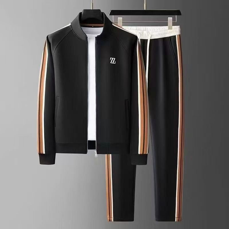 Tuta sportiva nera con strisce laterali marroni e bianche, giacca con zip e pantaloni abbinati, appesa su grucce. Abbigliamento casual elegante.