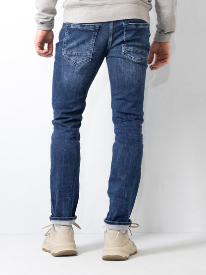 Jeans uomo slim fit blu, visti da dietro, abbinati a scarpe sportive beige e felpa grigia. Moda casual maschile, abbigliamento denim.