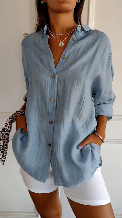 Donna con camicia azzurra in lino, maniche lunghe, abbinata a pantaloncini bianchi. Stile casual estivo, accessori minimalisti.