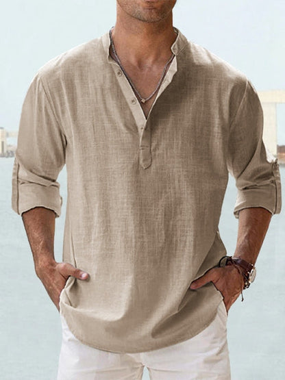 Camicia uomo lino beige, maniche lunghe arrotolate, stile casual estivo, colletto alla coreana, abbinata a pantaloni bianchi.