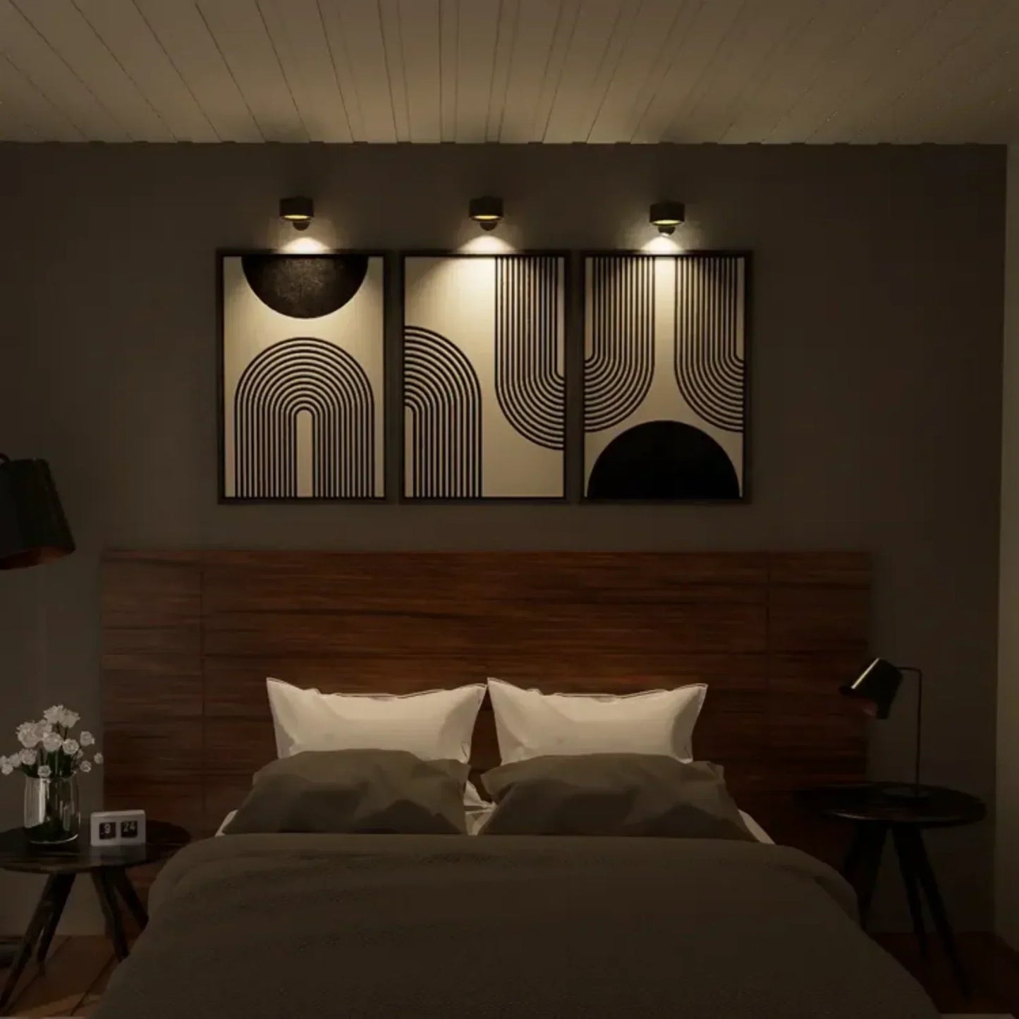 Camera da letto moderna con letto matrimoniale, testiera in legno, cuscini bianchi, coperta grigia, quadri astratti e illuminazione soffusa.