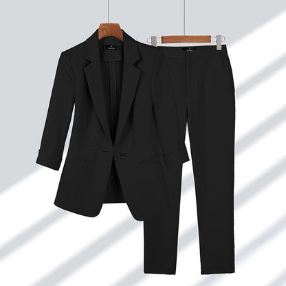 Completo elegante nero da donna, giacca e pantaloni abbinati, appesi su grucce di legno. Moda formale, abbigliamento da ufficio.