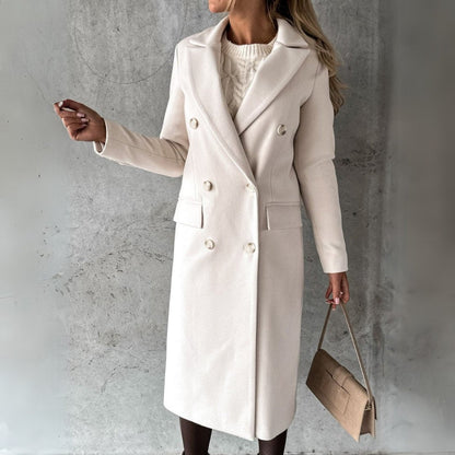 Donna con cappotto bianco elegante, doppio petto, in posa contro parete grigia. Moda autunno inverno, borsa beige, stile sofisticato.