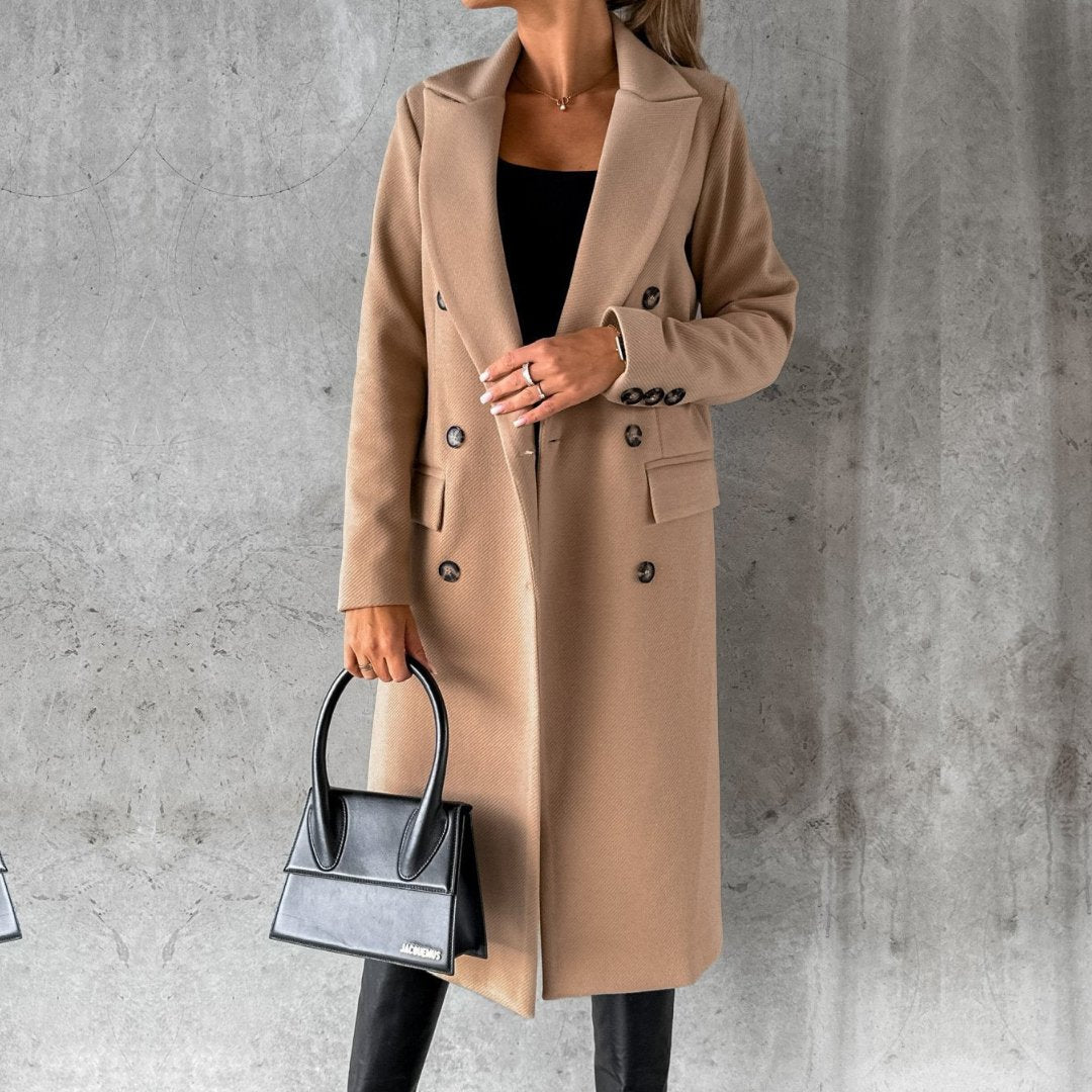 Donna con cappotto cammello elegante, borsa nera di design, sfondo grigio. Moda autunnale, stile sofisticato, tendenze abbigliamento femminile.