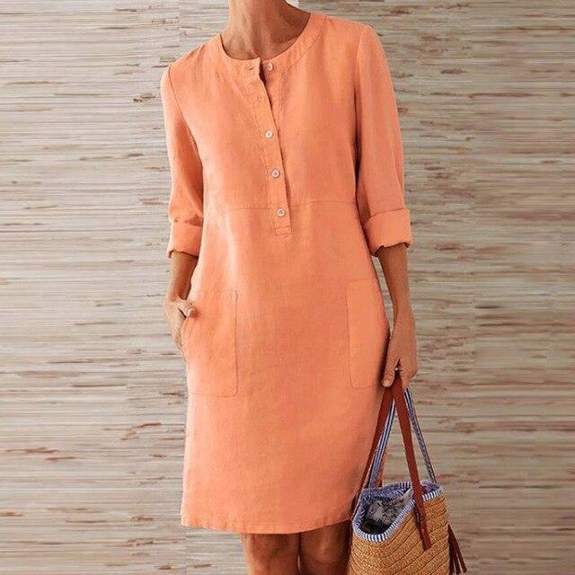 Donna con abito di lino arancione, maniche lunghe, tasche frontali, tiene una borsa di paglia. Moda estiva casual, abbigliamento femminile elegante.