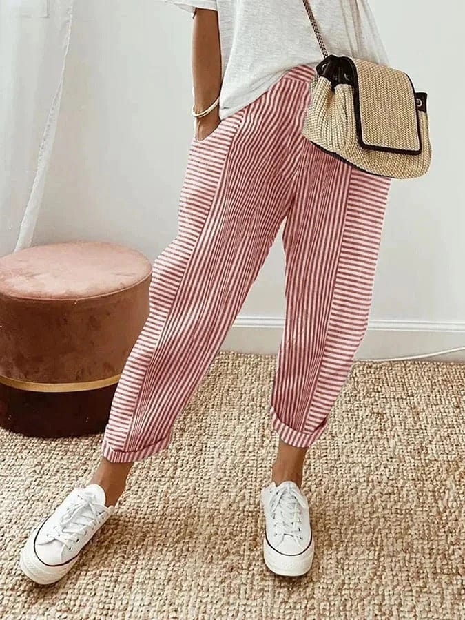 Donna con pantaloni a righe rosse e bianche, borsa a tracolla in paglia, maglietta bianca, scarpe da ginnastica bianche su tappeto beige.