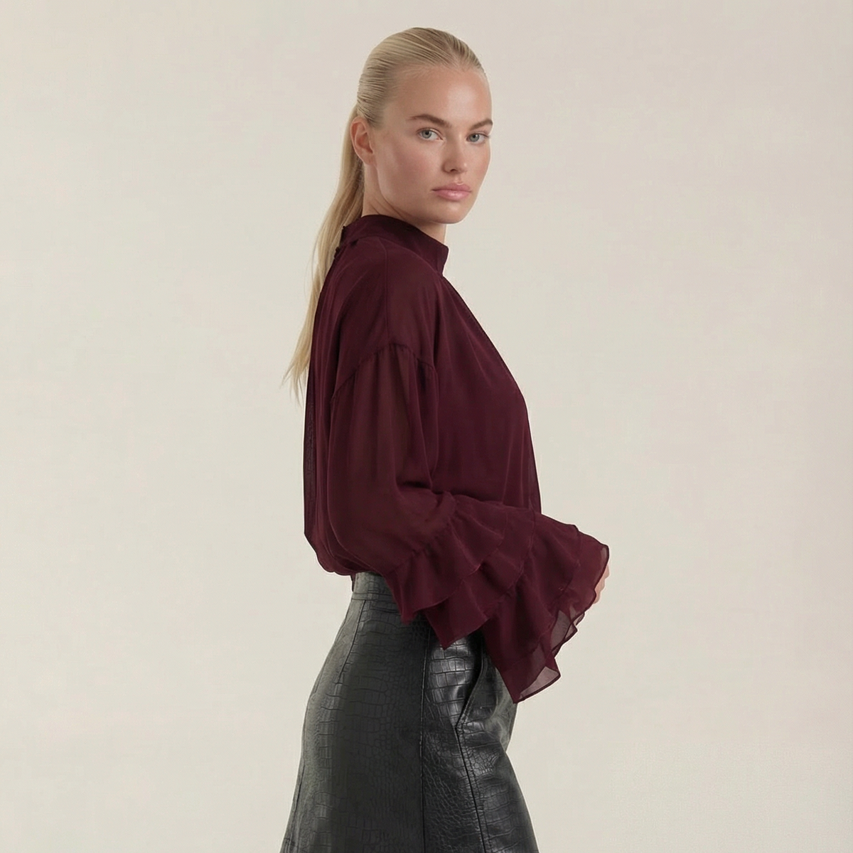 Blusa de mujer color burdeos de gasa transparente con mangas con volantes y cuello alto.