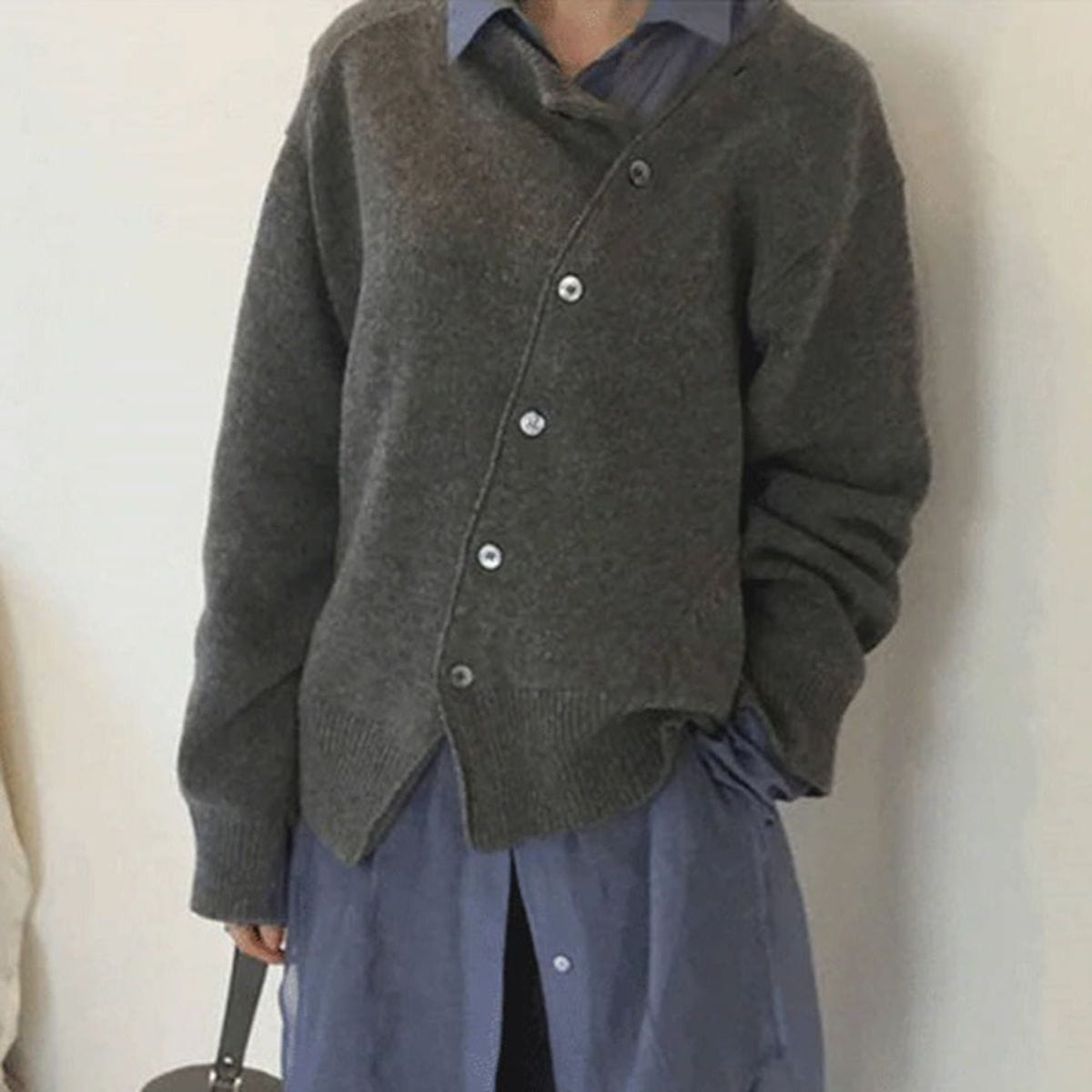Donna con cardigan grigio asimmetrico sopra camicia blu, moda autunnale, abbigliamento casual elegante, stile minimalista.