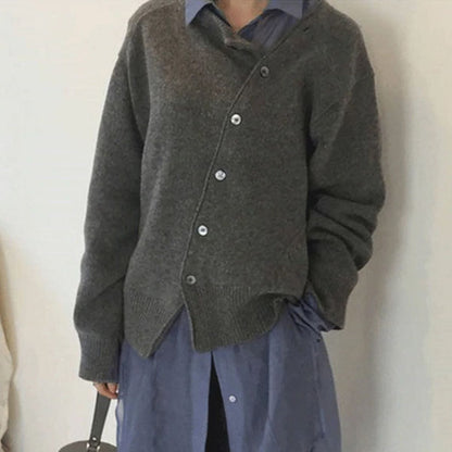 Donna con cardigan grigio asimmetrico sopra camicia blu, moda autunnale, abbigliamento casual elegante, stile minimalista.