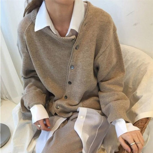 Donna con cardigan beige e camicia bianca, seduta su sedia. Moda autunnale elegante, abbigliamento casual chic, tendenze moda 2023.